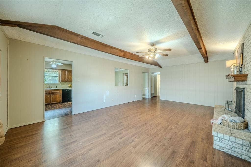 1517 Meadow Court, Midlothian, TX 76065 Spacious living area featuring wood-finish flooring, exposed ceiling beams, a ceiling fan, and a brick fireplace with a wood mantle