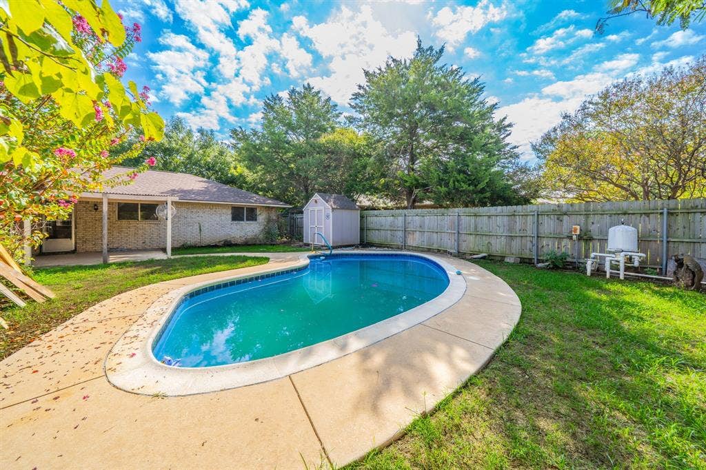 1517 Meadow Court, Midlothian, TX 76065 Backyard featuring a curved inground swimming pool with a concrete surround, a covered patio, and a storage shed
