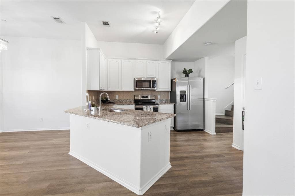 Kitchen island with a granite countertop and an undermount sink, white cabinetry with stainless steel appliances, and wood-finish flooring