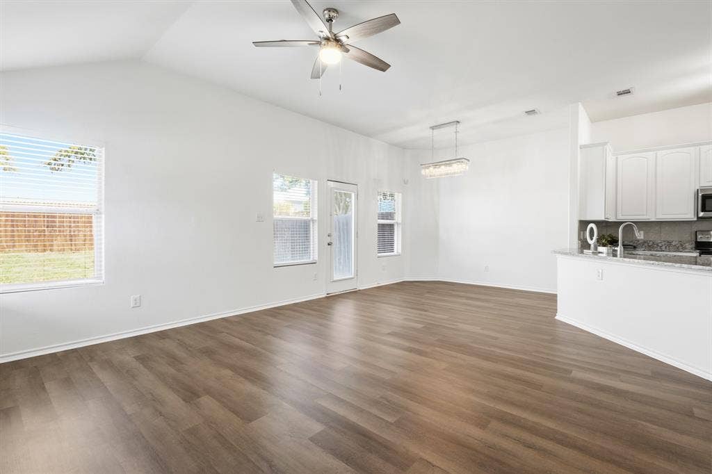 Vaulted ceiling with a contemporary ceiling fan, wood-finish flooring, white cabinetry, granite countertops, and stainless steel appliances