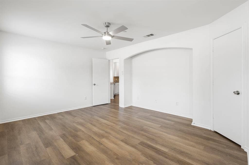Wood-finish flooring, ceiling fan with integrated lighting, arched wall niche, and white interior doors