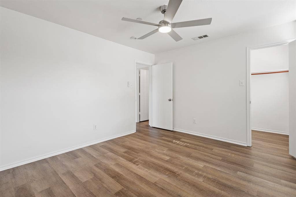 Wood-finish flooring, white painted walls, and a ceiling fan with integrated lighting