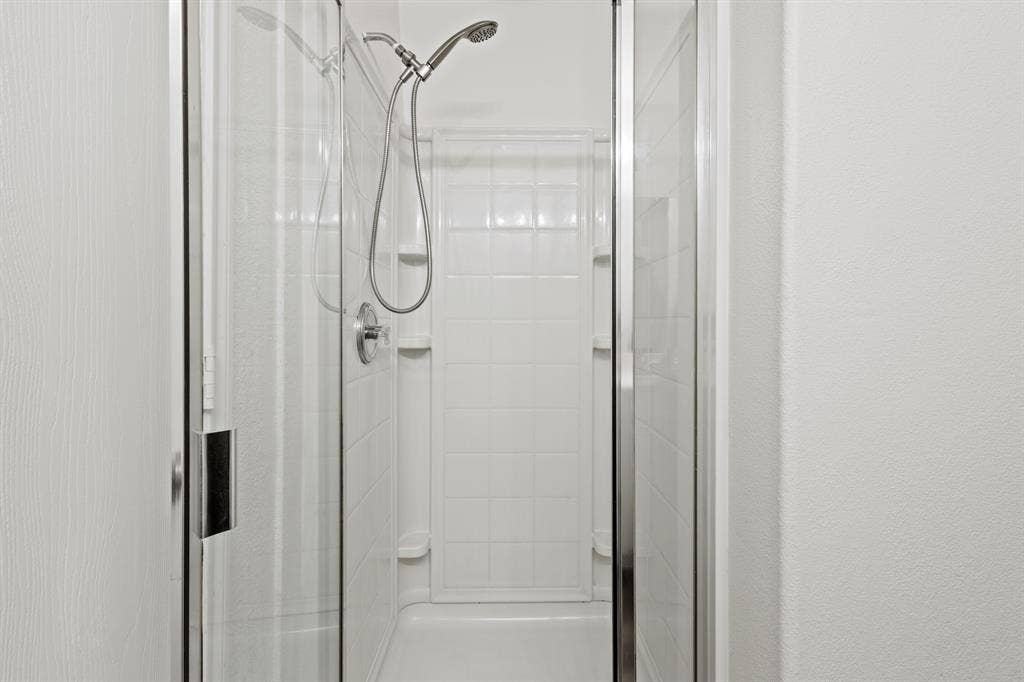 Shower enclosure with clear glass doors, white tiled walls, and a chrome shower fixture