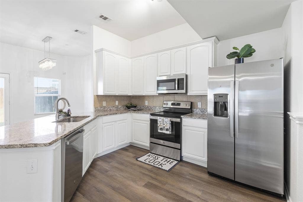 White cabinetry, stainless steel appliances, granite countertops, wood-finish flooring, and a decorative pendant light fixture