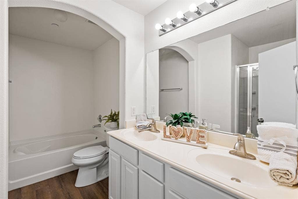 Double vanity with undermount sinks, wood-finish flooring, and a bath/shower combination in the primary bedroomn