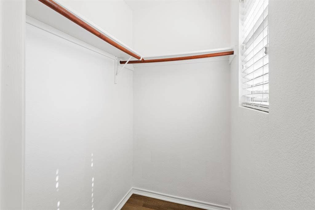 Walk-in closet with wood-finish flooring, white walls, built-in shelving, and a window with horizontal blinds