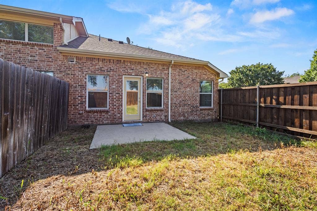 Brick exterior with multiple windows and a rear door, complemented by a concrete patio slab and wood privacy fencing