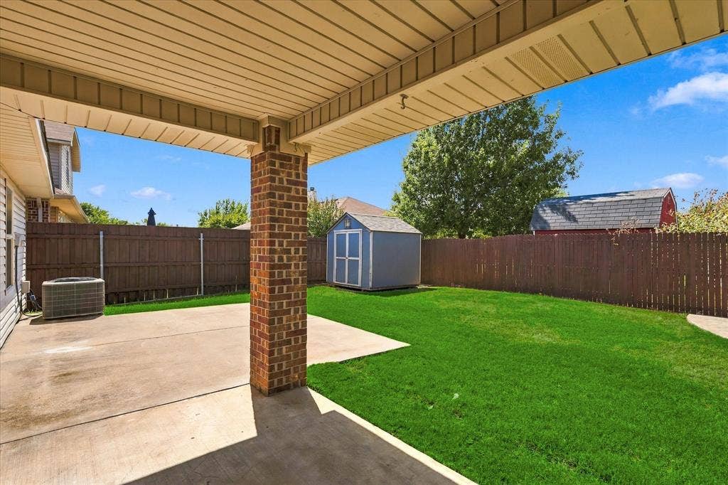 4516 Remuda Lane, Denton, TX 76226 Covered patio with a brick pillar, concrete patio area, and expansive green lawn