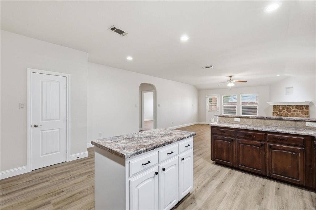 4516 Remuda Lane, Denton, TX 76226 Wood-finish flooring throughout, kitchen island with cabinet storage, stone-look countertops, dark wood-finish cabinetry, and a stone-clad fireplace