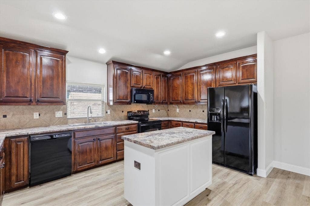 4516 Remuda Lane, Denton, TX 76226 Kitchen featuring wood-finish cabinetry, light-toned countertops, a central island, and black appliances