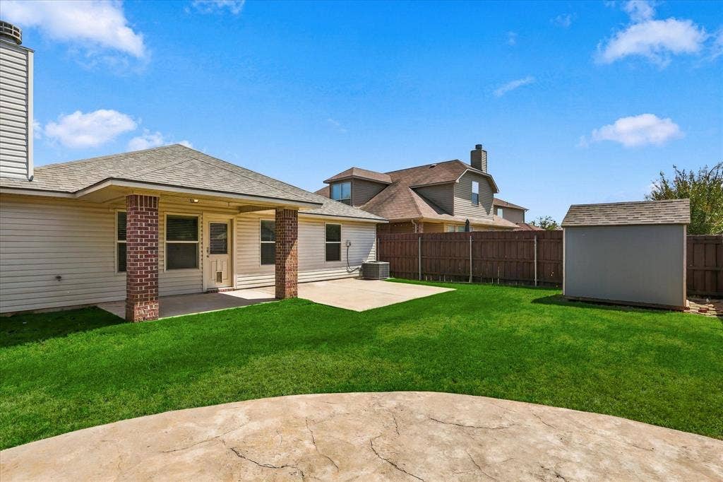 4516 Remuda Lane, Denton, TX 76226 Expansive backyard featuring a manicured lawn, concrete patio, and a storage shed
