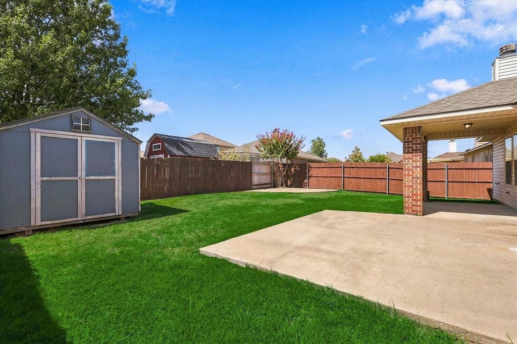 4516 Remuda Lane, Denton, TX 76226 Expansive fenced backyard featuring a storage shed, concrete patio, and lush lawn