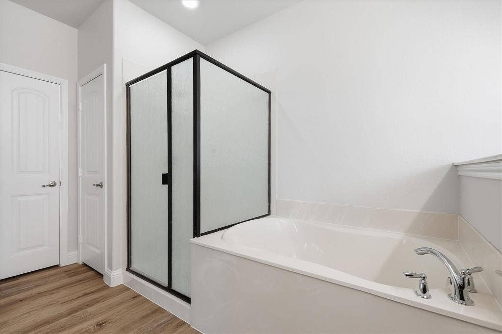 4516 Remuda Lane, Denton, TX 76226 Soaking tub with chrome fixtures, enclosed shower with a black frame and frosted glass, wood-finish flooring, and white paneled doors