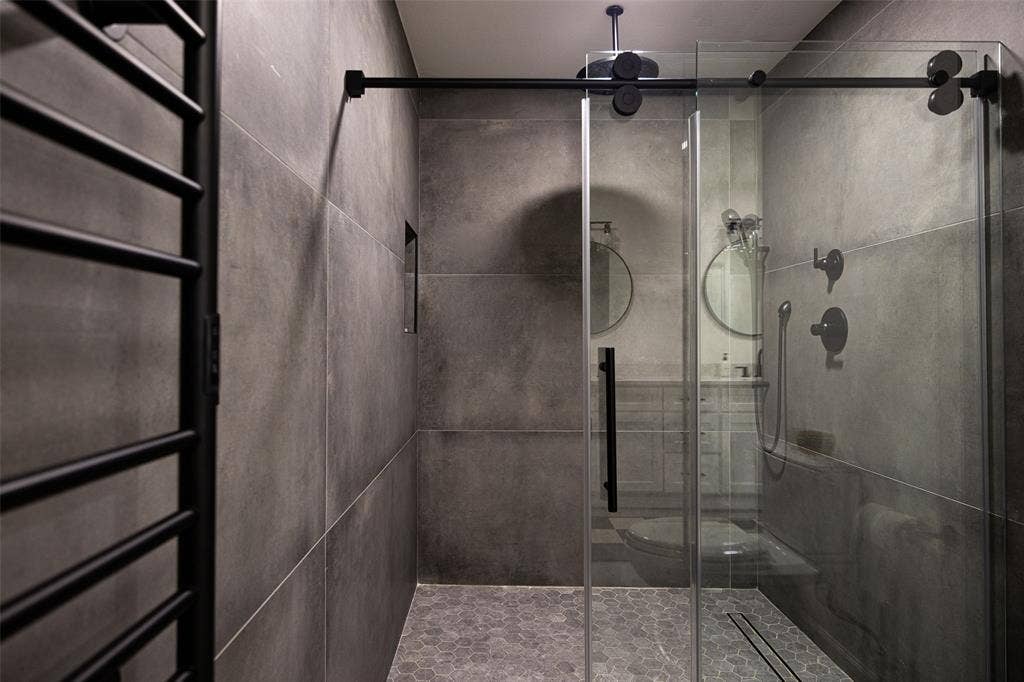 Shower enclosure with sliding glass door, matte black fixtures, full-height wall tiling, and hexagonal floor tiling