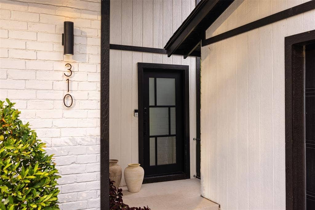 White painted brick facade with a black cylindrical outdoor light fixture, contrasting black window trim, and a black paneled door with frosted glass inserts