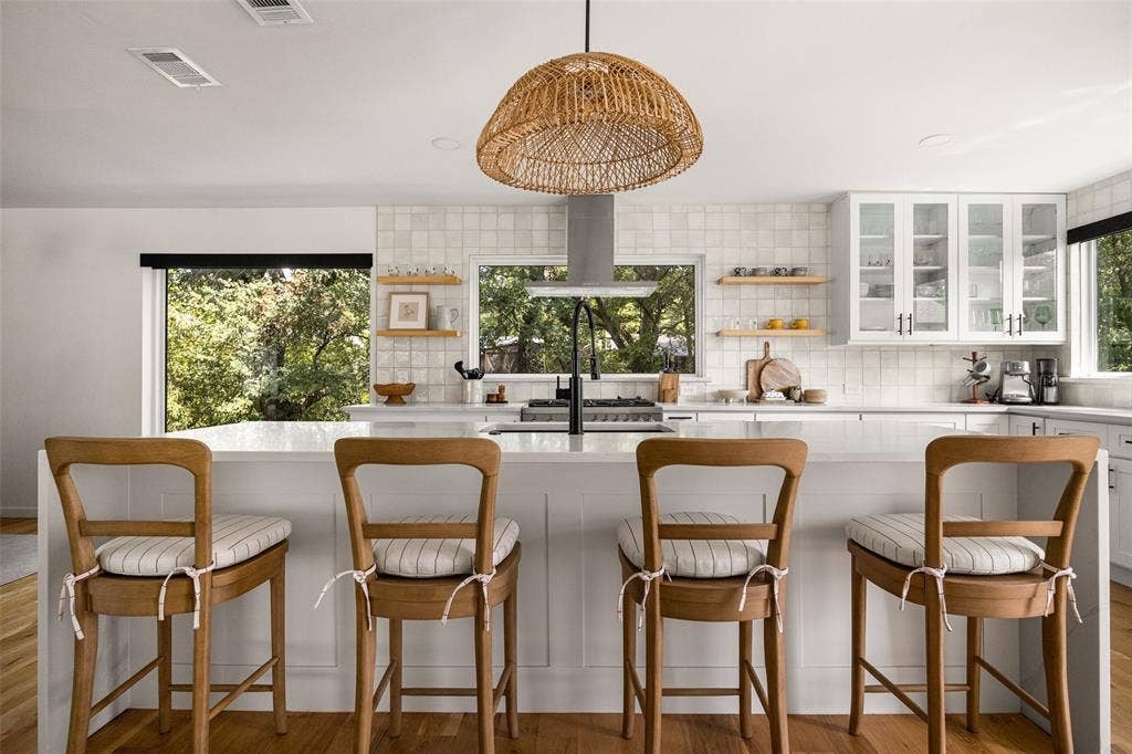 Kitchen featuring white cabinetry, light-toned backsplash tiling, a built-in range hood, and a woven pendant light fixture