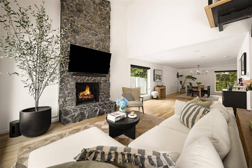 Vaulted ceilings with recessed lighting, stone-finish fireplace, wood-finish flooring, and large windows