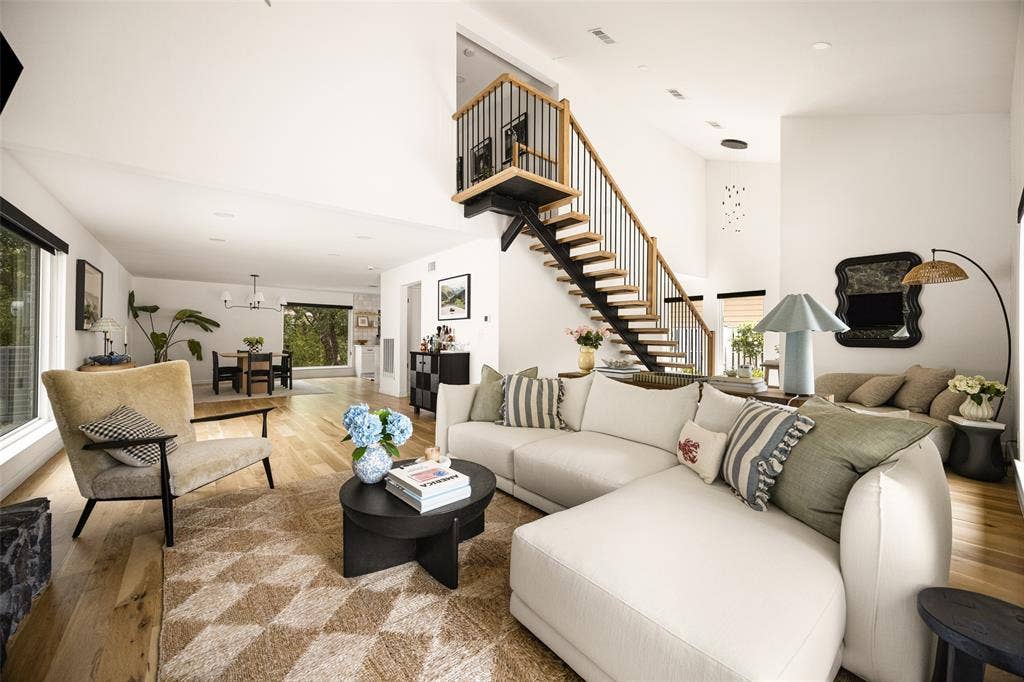 Open-concept living area with wood-finish flooring, a contemporary staircase featuring black spindles and wood handrails, and large windows providing abundant light