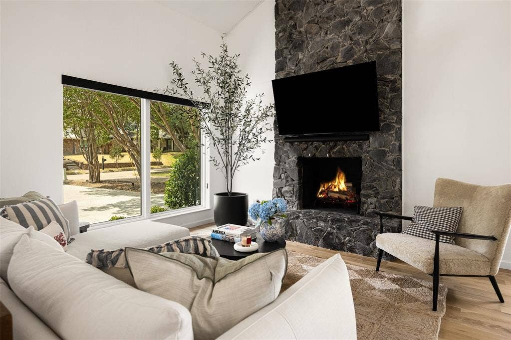 Expansive floor-to-ceiling windows, stone-clad fireplace with hearth, and light wood-finish flooring