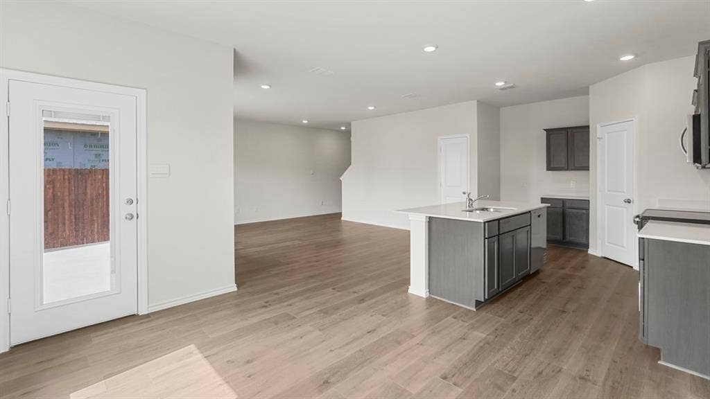 Contemporary kitchen and living area featuring wood-finish flooring, recessed lighting, and a kitchen island with an integrated sink and light-toned countertop