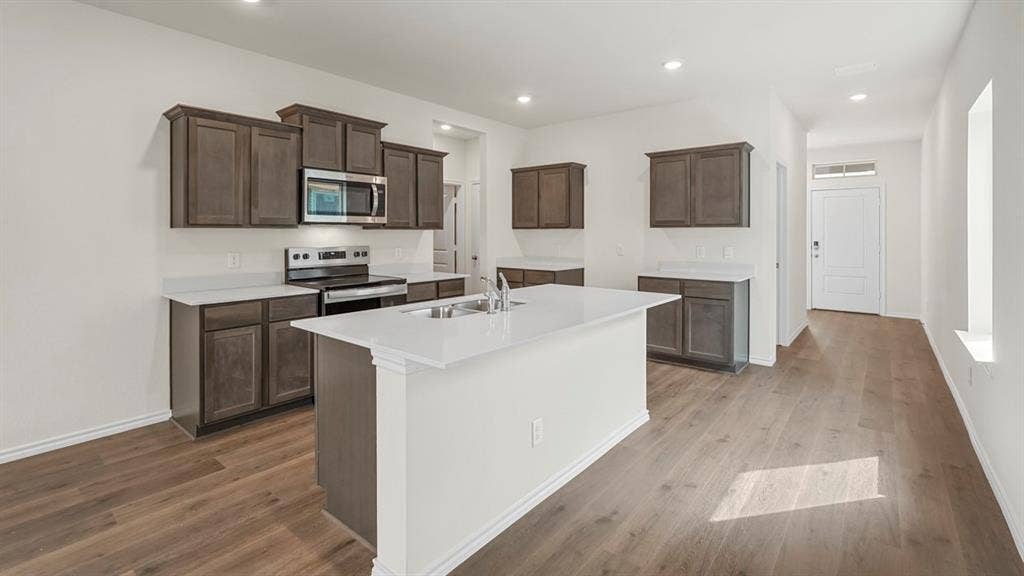 Kitchen featuring an island with a double basin sink, stainless steel appliances, dark wood-finish cabinetry, and light countertops