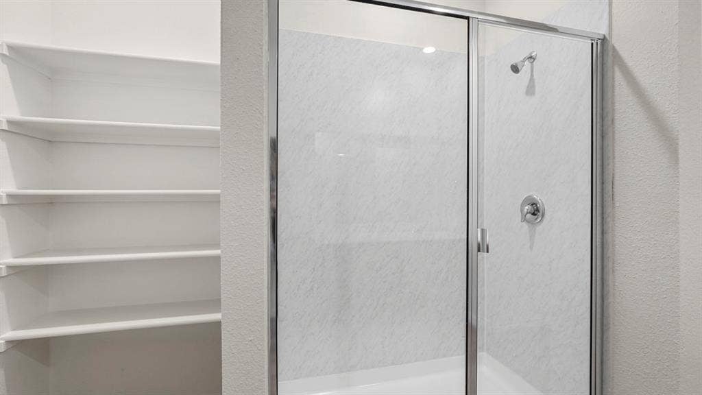 Shower enclosure with clear glass doors and a white marble-look surround, featuring a chrome shower head and handle