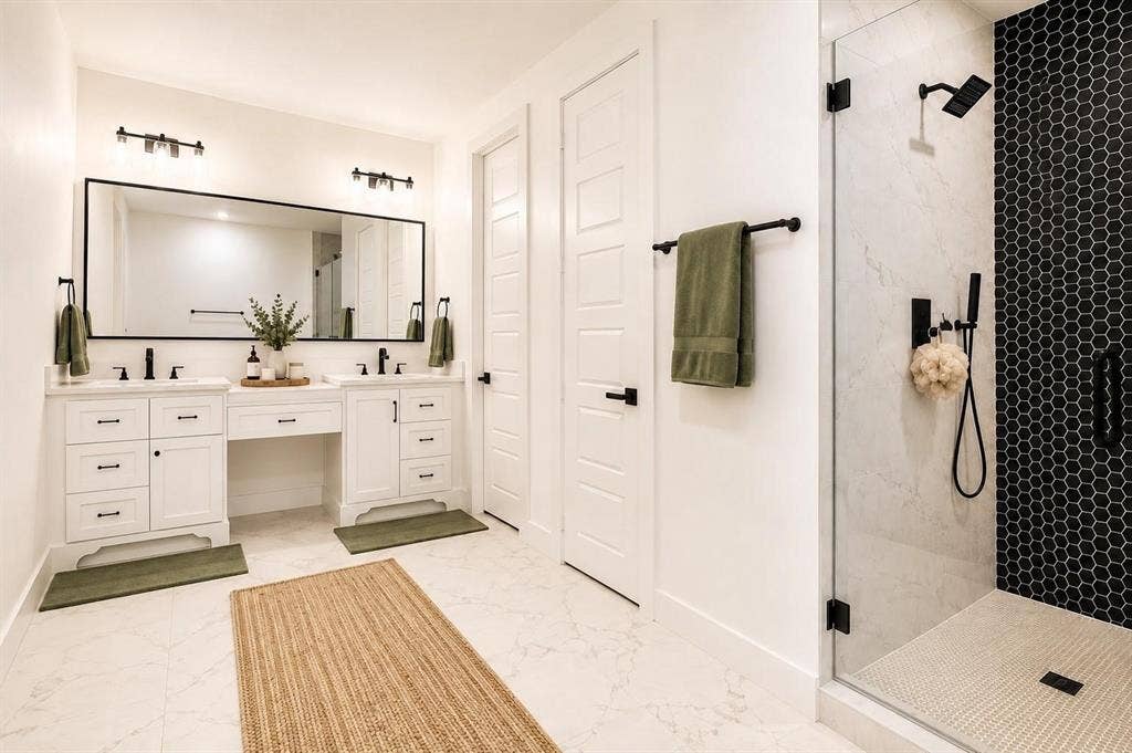 713 Wayne Street, Dallas, TX 75223 Dual vanities with white cabinetry and dark hardware, large frameless mirror, walk-in shower with black hexagonal tile accent, glass shower enclosure, and light-toned floor tiling
