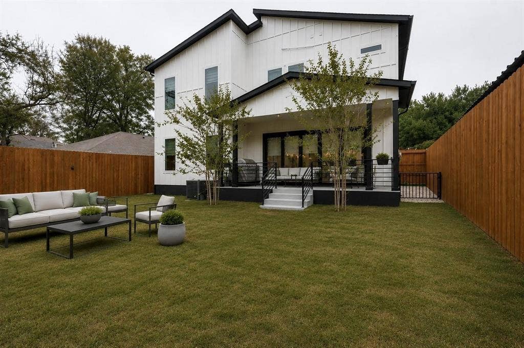 713 Wayne Street, Dallas, TX 75223 Expansive green lawn with a newly installed wood privacy fence, a covered patio with black railing, and a modern white and black exterior