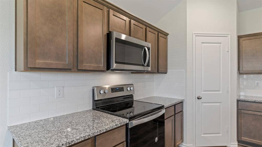 223 Yates Street, Bullard, TX 75757 Kitchen featuring wood-finish cabinetry, granite countertops, white subway tile backsplash, and stainless steel appliances