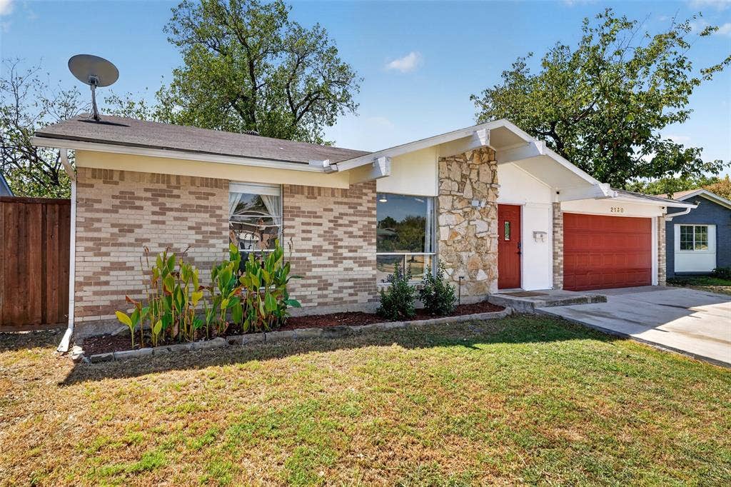 2130 Bowie Drive, Carrollton, TX 75006 Brick and stone exterior with a prominent red garage door, a concrete driveway, and established landscaping
