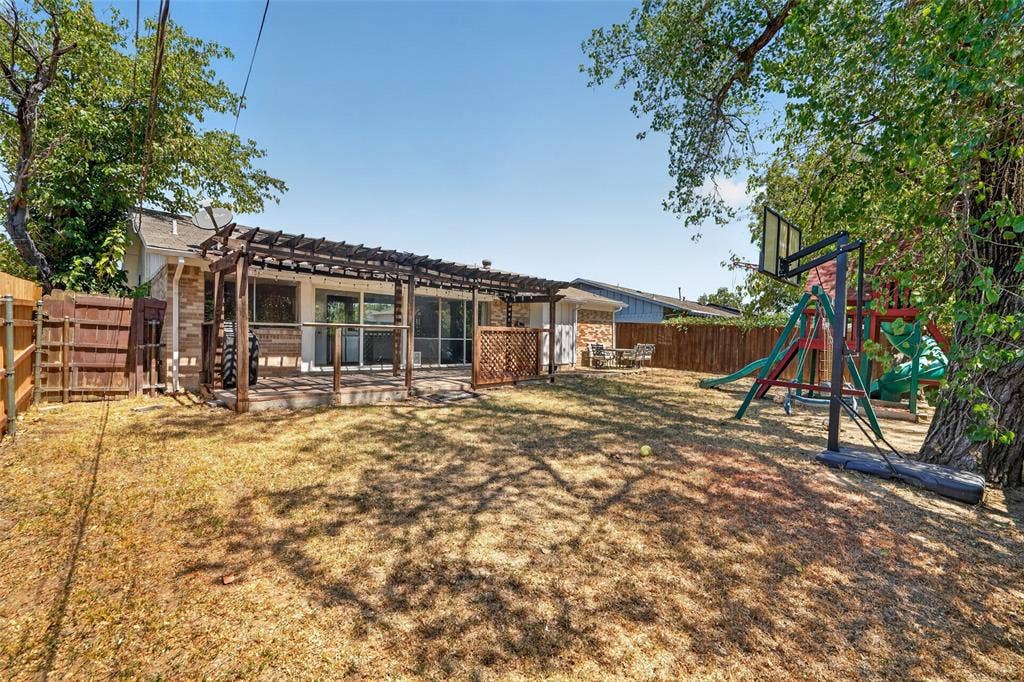 2130 Bowie Drive, Carrollton, TX 75006 Expansive backyard featuring a wood privacy fence, mature trees, and a pergola-covered patio
