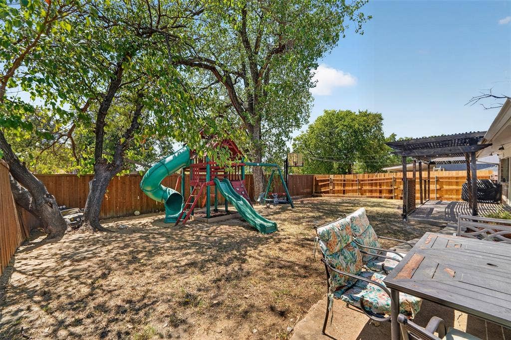 2130 Bowie Drive, Carrollton, TX 75006 Expansive backyard featuring mature trees, a wood privacy fence, and an attached concrete patio with a dark-finish pergola