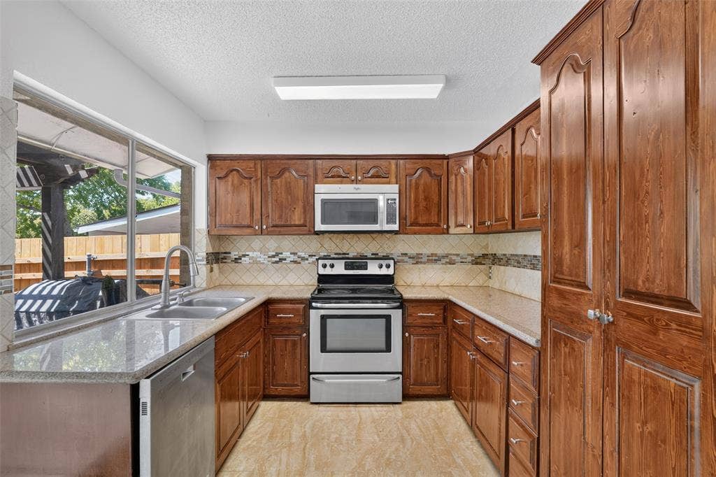 2130 Bowie Drive, Carrollton, TX 75006 Spacious kitchen featuring extensive wood cabinetry, stainless steel appliances, a double basin sink, and a large window