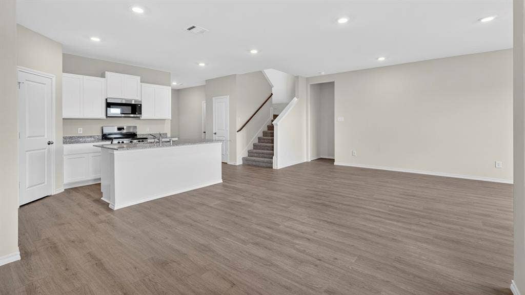 237 Yates Street, Bullard, TX 75757 Open-concept living space featuring wood-finish flooring, recessed lighting, and a kitchen with white cabinetry, stainless steel appliances, and a central island with a granite-style countertop