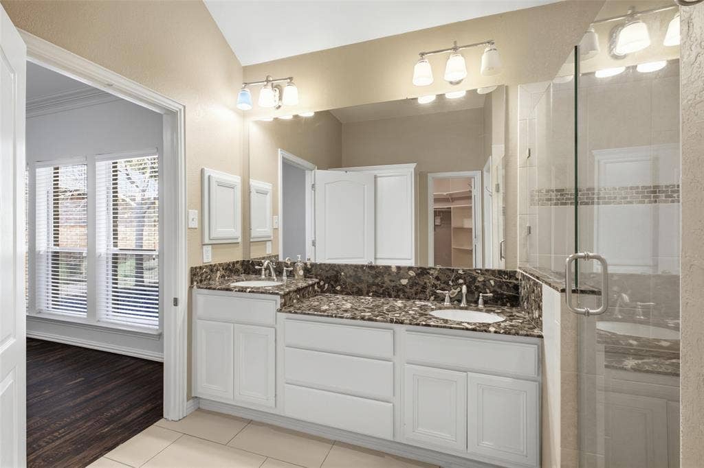 14616 Vintage Lane, Addison, TX 75001 Dual vanity with undermount sinks, stone countertop, white cabinetry, and glass-enclosed shower