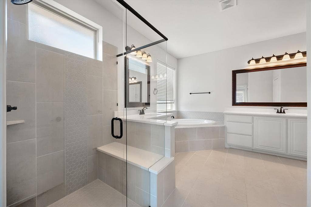 5626 Rutherford Drive, Midlothian, TX 76065 This bathroom is a showstopper — a glass walk-in shower with hexagon tile detail, a deep soaking tub tucked under the window, and dual vanities so you never have to share sink space.