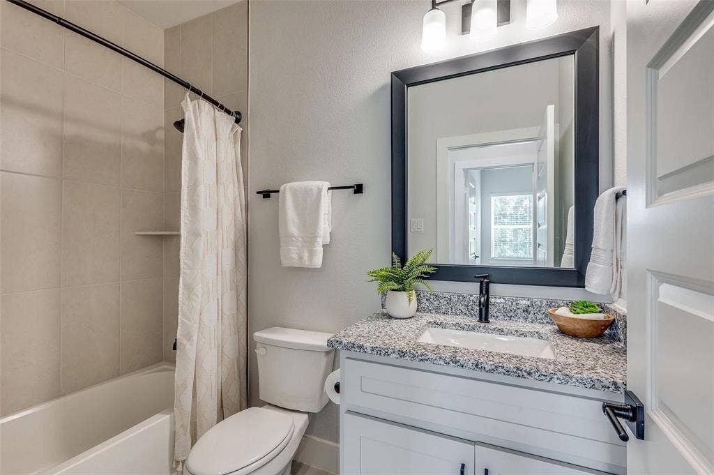 505 Mission Trail, #603, Arlington, TX 76010 White paneled door, black-framed mirror, granite countertop, white vanity with black hardware, and a tiled shower surround