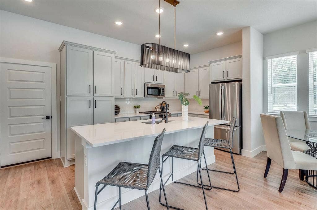505 Mission Trail, #603, Arlington, TX 76010 Contemporary kitchen featuring light wood-finish flooring, white cabinetry, integrated stainless steel appliances, and an island with a white countertop