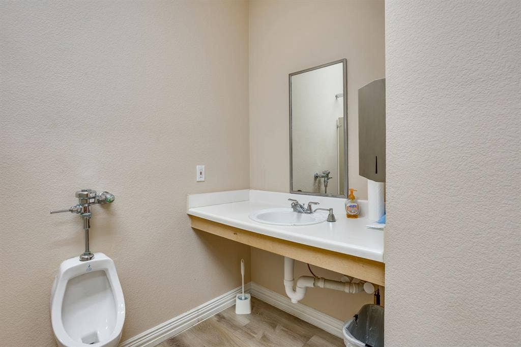 1415 E Belt Line Road, Carrollton, TX 75006 White wall-mounted urinal, single basin sink, laminate countertop, and wood-finish flooring