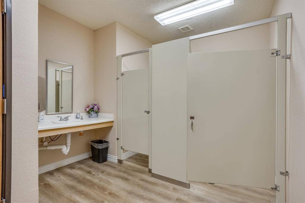 1415 E Belt Line Road, Carrollton, TX 75006 Restroom featuring wood-finish flooring, a white vanity with an integrated sink, a rectangular framed mirror, and partition stalls