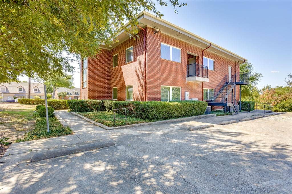 1415 E Belt Line Road, Carrollton, TX 75006 Brick exterior with multiple windows, second-story balcony with metal railing, exterior metal staircase, and an asphalt parking area