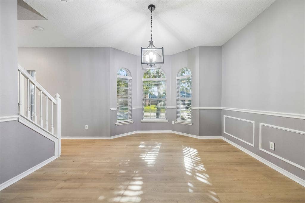 753 Summerfield Drive, Allen, TX 75002 Vaulted ceiling featuring a decorative chandelier, multiple arched windows with blinds, wainscoting details, wood-finish flooring, and staircase with white banister