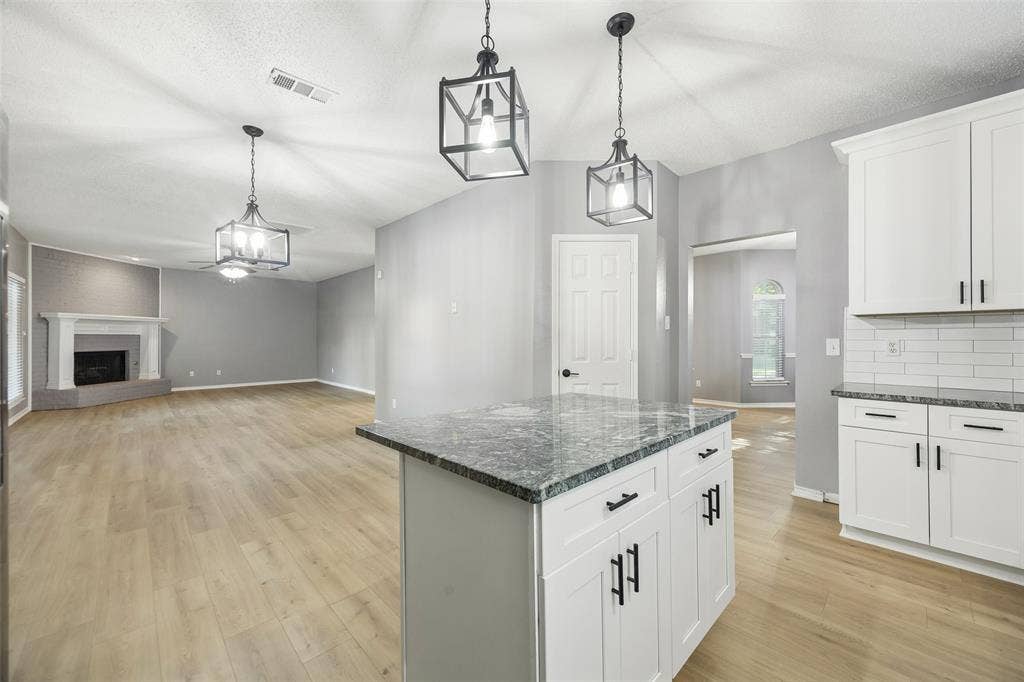 753 Summerfield Drive, Allen, TX 75002 Kitchen island with stone countertop and white cabinetry, wood-finish flooring, white subway tile backsplash, and a corner fireplace with a white mantel