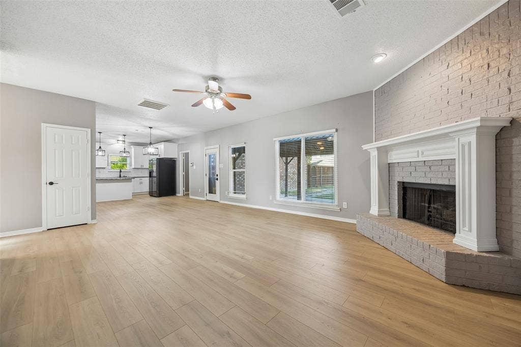 753 Summerfield Drive, Allen, TX 75002 Spacious living area featuring wood-finish flooring, a painted brick fireplace with a white mantel, and a ceiling fan