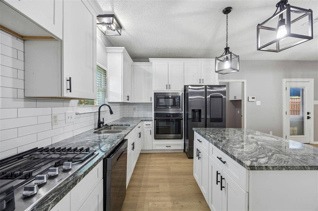 753 Summerfield Drive, Allen, TX 75002 White cabinetry with matte black hardware, integrated stainless steel appliances, wood-finish flooring, and a large central island with a patterned countertop