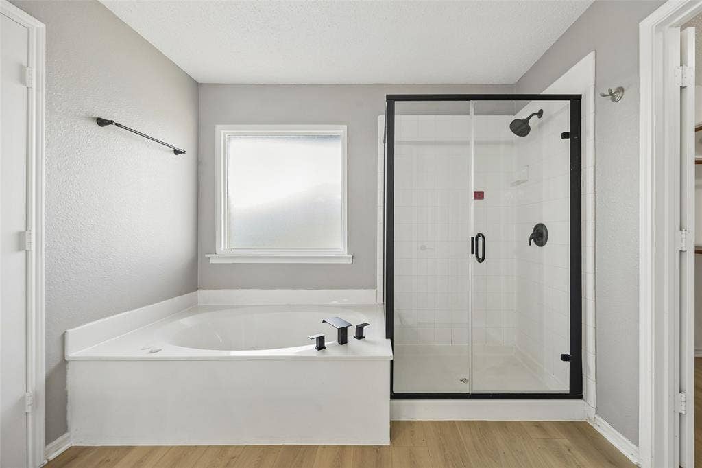 753 Summerfield Drive, Allen, TX 75002 Soaking tub with black fixtures, enclosed shower with black frame, white subway tile shower surround, and wood-finish flooring