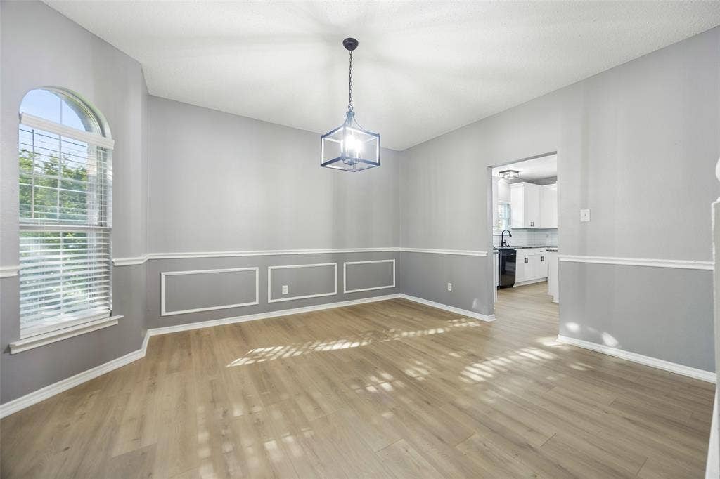 753 Summerfield Drive, Allen, TX 75002 Wood-finish flooring, accent wall paneling, vaulted ceiling, arched window, and a contemporary light fixture