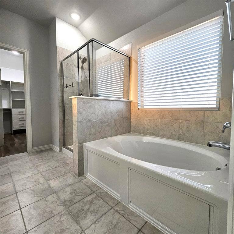 2225 Crooked Bow Drive, Mesquite, TX 75149 Tile flooring, built-in soaking tub, glass-enclosed shower, tiled half-wall, and a window with blinds