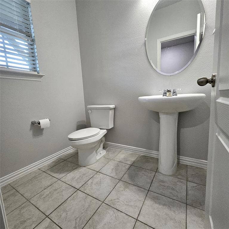 2225 Crooked Bow Drive, Mesquite, TX 75149 White pedestal sink with chrome faucet, white toilet, oval wall mirror, and tile flooring