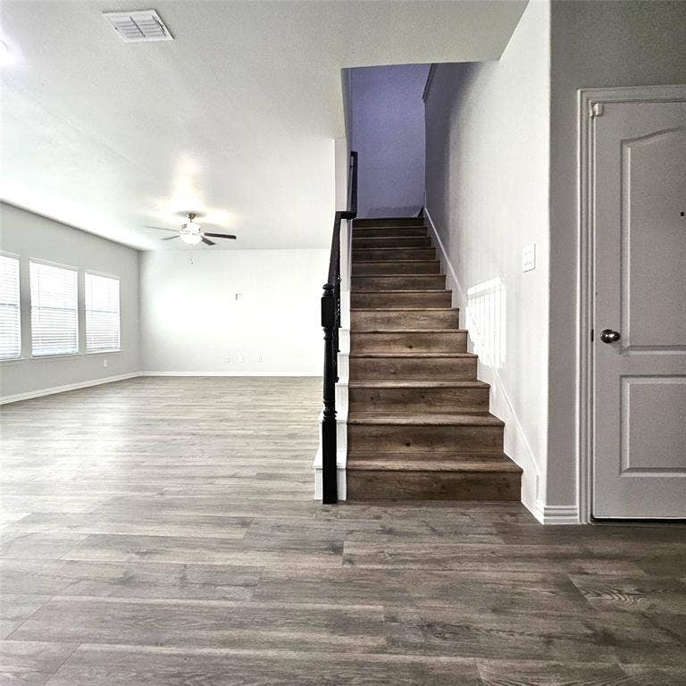2225 Crooked Bow Drive, Mesquite, TX 75149 Spacious living area featuring wood-finish flooring, multiple windows with blinds, a ceiling fan, and a staircase with a dark wood-finish handrail